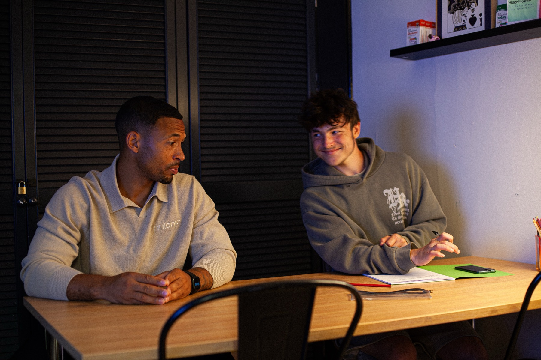 A mentor and a teenage student talking across a desk